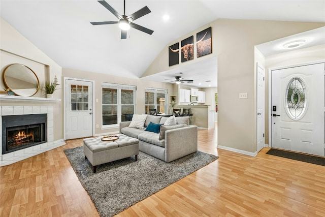 living area with baseboards, a tile fireplace, light wood-type flooring, a ceiling fan, and high vaulted ceiling
