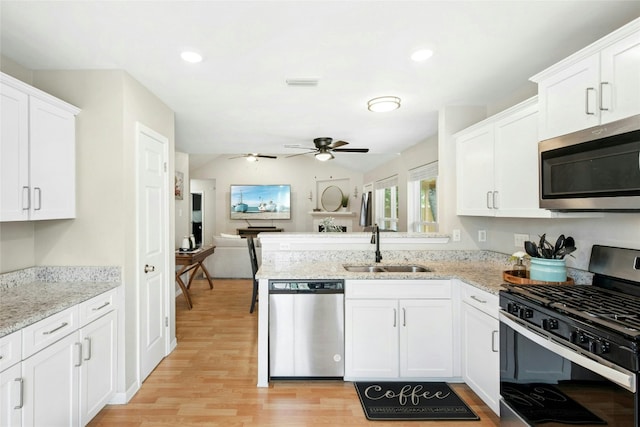 kitchen featuring stainless steel appliances, light wood finished floors, a sink, white cabinetry, and a peninsula