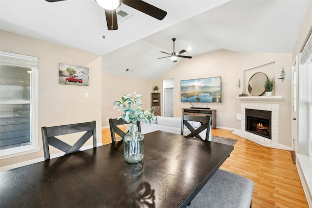 dining area featuring lofted ceiling, a ceiling fan, a tile fireplace, and light wood-style flooring