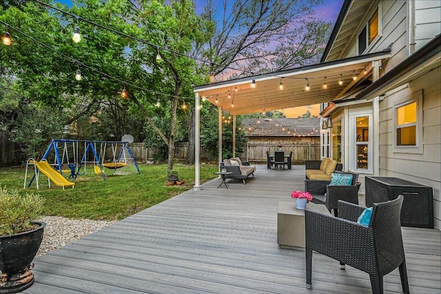 deck at dusk with a playground, a lawn, and a fenced backyard