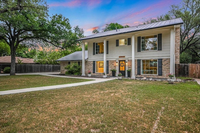 neoclassical home with fence, metal roof, a lawn, brick siding, and a standing seam roof