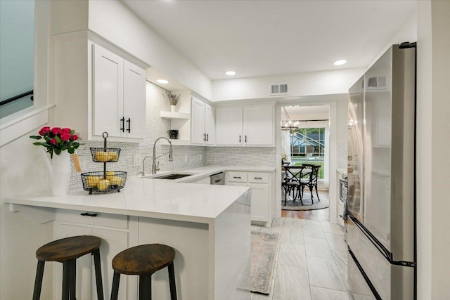 kitchen with a sink, a peninsula, open shelves, visible vents, and appliances with stainless steel finishes