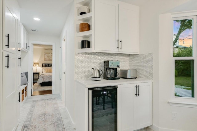 bar with tasteful backsplash, visible vents, light wood-style flooring, beverage cooler, and baseboards