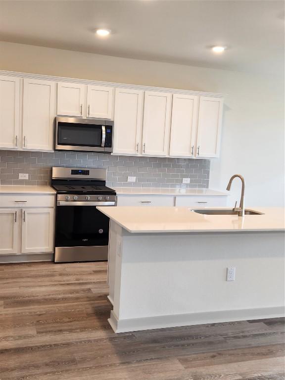 7500 Traylor Cv, Austin, TX 78724 - kitchen with stainless steel appliances, a sink, white cabinets, light countertops, and wood finished floors