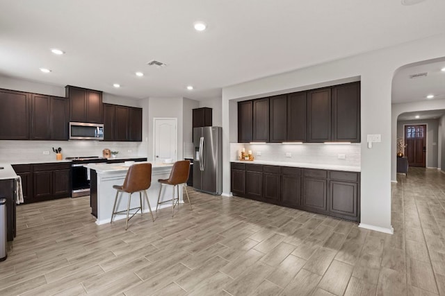 330 Conestoga Dr, Kyle, TX 78640 - kitchen featuring appliances with stainless steel finishes, arched walkways, decorative backsplash, light wood finished floors, and recessed lighting