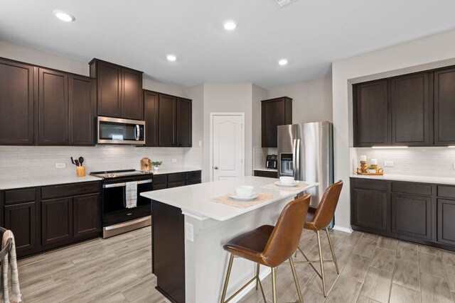 330 Conestoga Dr, Kyle, TX 78640 - kitchen featuring appliances with stainless steel finishes, a breakfast bar area, light countertops, dark brown cabinetry, and recessed lighting