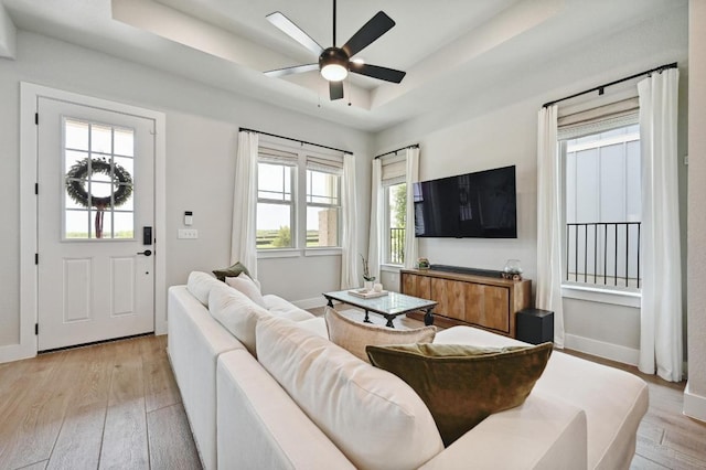 living room featuring a tray ceiling, a ceiling fan, baseboards, and light wood-type flooring