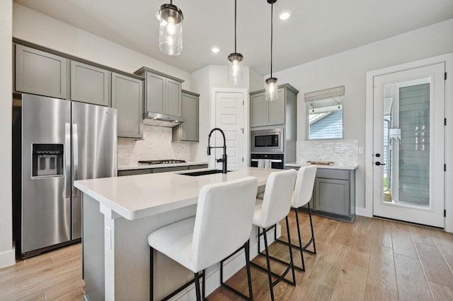 kitchen featuring tasteful backsplash, gray cabinets, light wood-style flooring, stainless steel appliances, and a sink