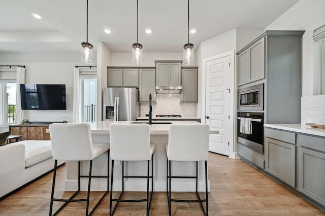 kitchen with gray cabinetry, open floor plan, backsplash, and stainless steel appliances