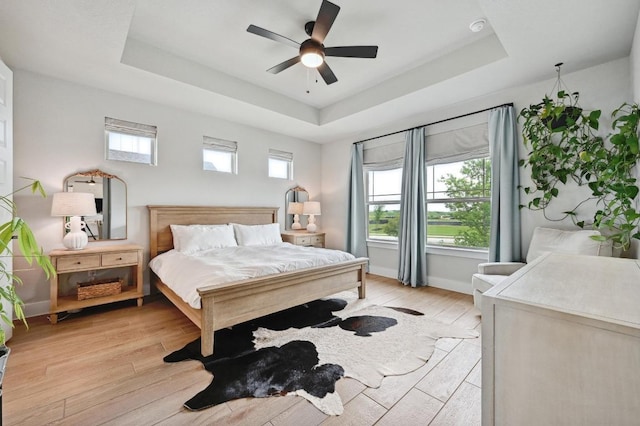 bedroom with multiple windows, baseboards, light wood-style floors, and a tray ceiling