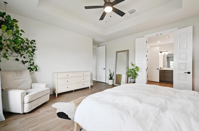 bedroom with visible vents, wood finished floors, ensuite bath, and a tray ceiling