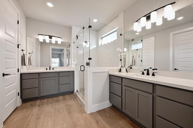 bathroom with two vanities, wood finished floors, a stall shower, and a sink