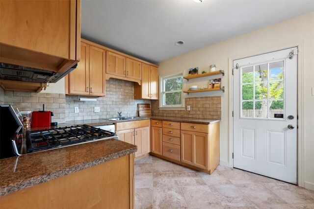kitchen featuring decorative backsplash, open shelves, gas range oven, dark countertops, and a sink