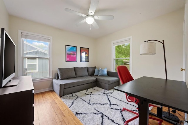 living room with baseboards, a ceiling fan, and light wood-style flooring