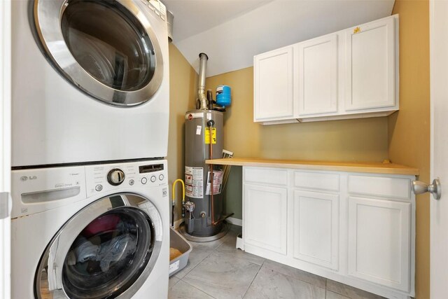 laundry area with gas water heater, cabinet space, stacked washer and clothes dryer, and light tile patterned floors