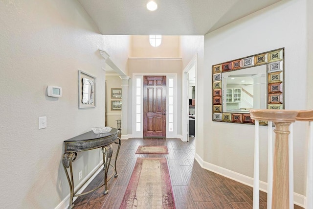 entrance foyer featuring decorative columns, a textured wall, dark wood-style floors, and baseboards