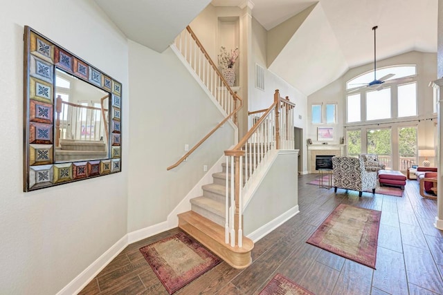 stairway featuring wood finished floors, a tiled fireplace, a ceiling fan, and visible vents