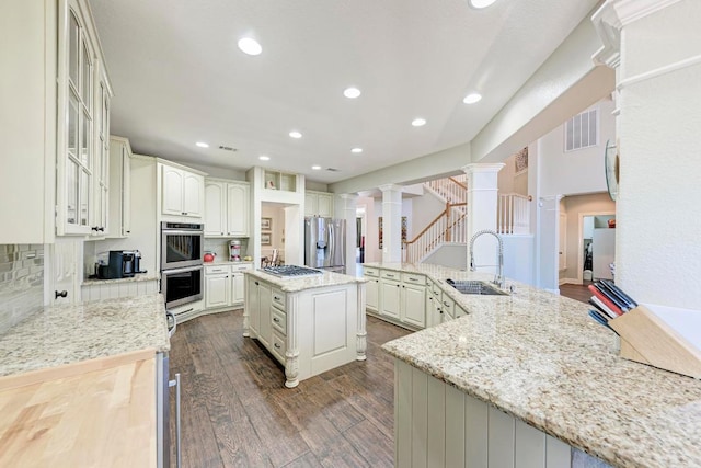 8236 Phantom Canyon Dr, Austin, TX 78726 - kitchen featuring decorative columns, appliances with stainless steel finishes, a large island, a sink, and dark wood-style flooring