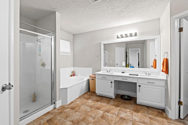 full bath featuring a textured ceiling, a sink, double vanity, a stall shower, and a garden tub