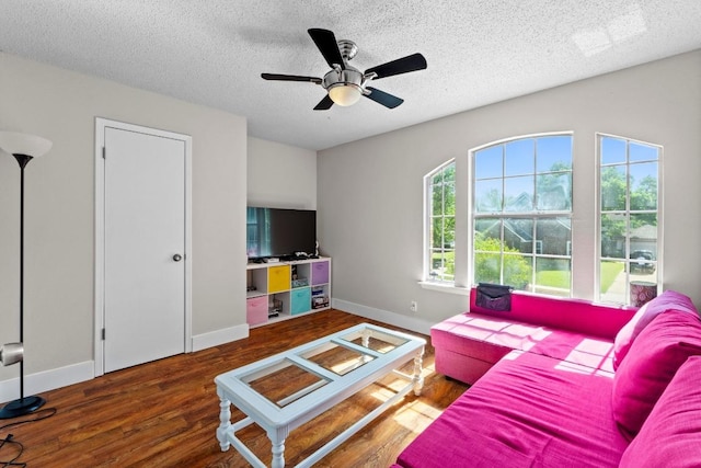 living room featuring a textured ceiling, ceiling fan, wood finished floors, and baseboards