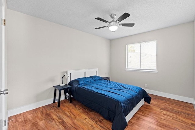 bedroom with baseboards, wood finished floors, a ceiling fan, and a textured ceiling