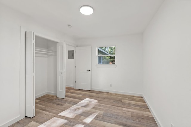 unfurnished bedroom with baseboards, wood finished floors, electric panel, and a closet