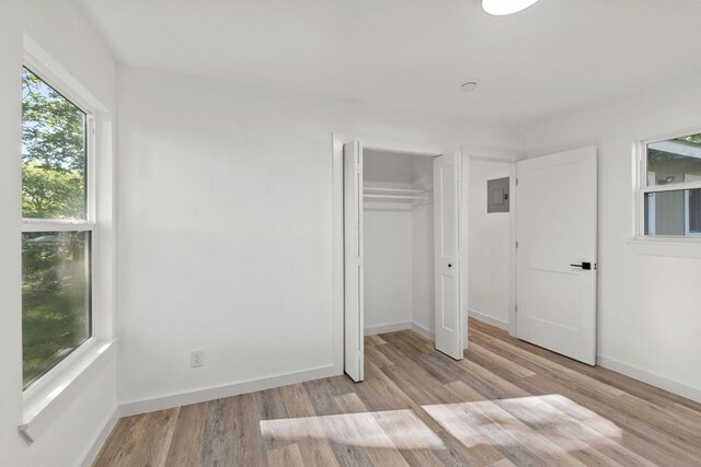 unfurnished bedroom with baseboards, wood finished floors, electric panel, and a closet
