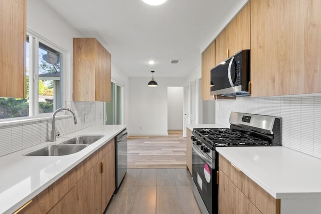 kitchen with decorative backsplash, stainless steel appliances, light countertops, light wood finished floors, and a sink