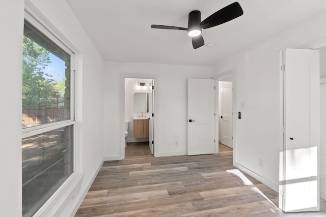 unfurnished bedroom with baseboards, ceiling fan, ensuite bath, and light wood-style flooring