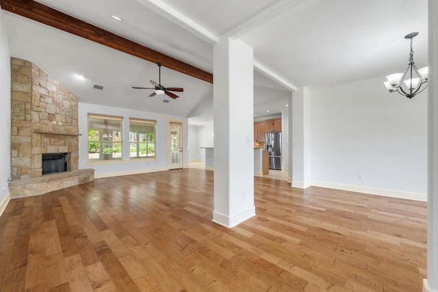 unfurnished living room with vaulted ceiling with beams, ceiling fan with notable chandelier, a stone fireplace, and light wood-style flooring