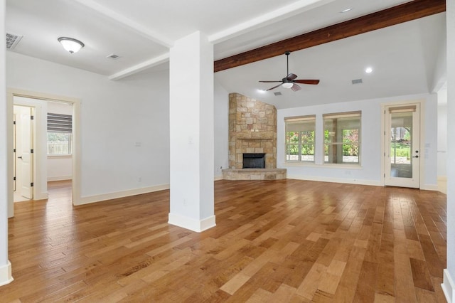 unfurnished living room featuring a wealth of natural light, vaulted ceiling with beams, ceiling fan, and a stone fireplace