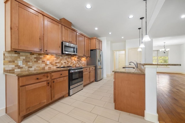 kitchen featuring decorative backsplash, a sink, stainless steel appliances, light stone countertops, and a notable chandelier