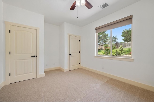 unfurnished bedroom featuring light colored carpet, visible vents, a ceiling fan, and baseboards