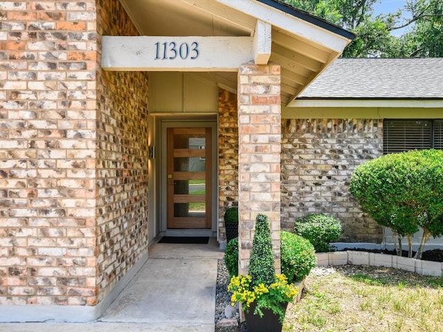 property entrance with a shingled roof and brick siding