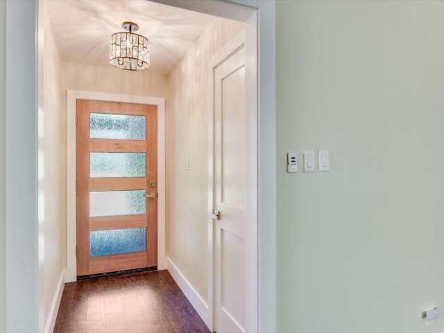 doorway featuring dark wood-style flooring, a notable chandelier, and baseboards
