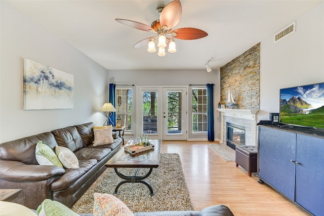 living area featuring visible vents, light wood-type flooring, a stone fireplace, and ceiling fan