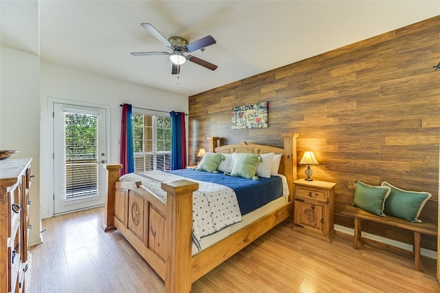 bedroom with light wood-style floors, access to outside, wooden walls, and ceiling fan
