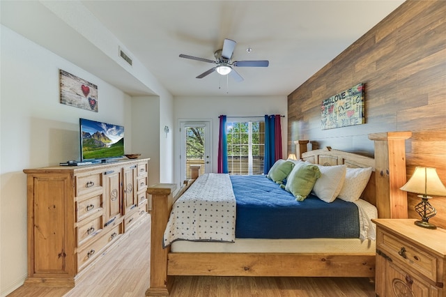 bedroom featuring visible vents, access to exterior, wooden walls, light wood-type flooring, and a ceiling fan