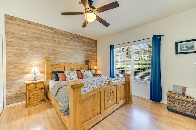 bedroom featuring wood walls, a ceiling fan, light wood finished floors, and baseboards