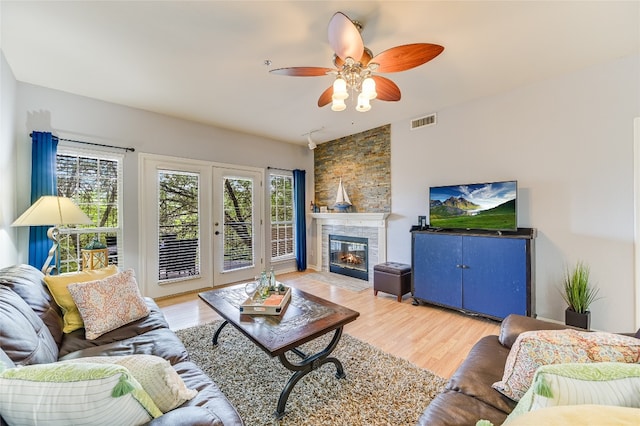 living area with a large fireplace, visible vents, ceiling fan, and light wood-style flooring
