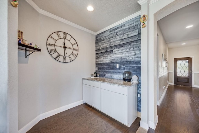 bar with dark wood finished floors, an accent wall, ornamental molding, and baseboards
