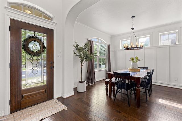 entryway with an inviting chandelier, dark wood-style flooring, a decorative wall, ornamental molding, and arched walkways