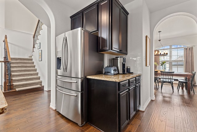 kitchen with light stone countertops, an inviting chandelier, stainless steel refrigerator with ice dispenser, and dark wood-style flooring