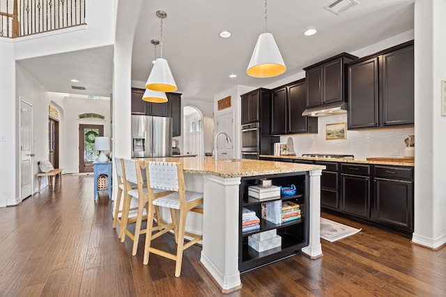 kitchen featuring decorative backsplash, appliances with stainless steel finishes, visible vents, light stone countertops, and a kitchen island with sink