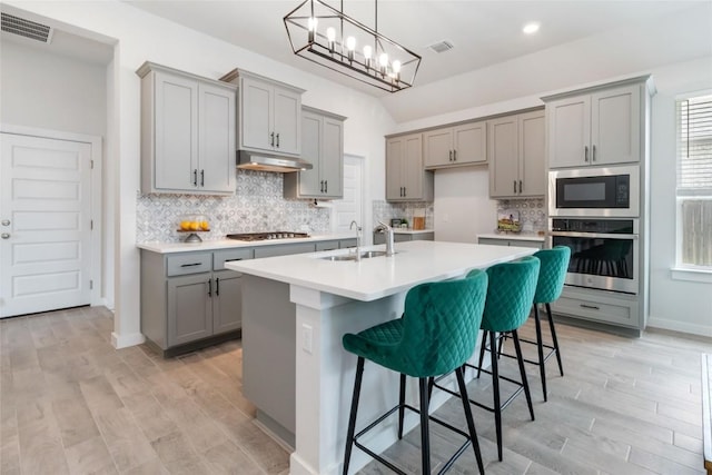 1109 Sweetspire St, Leander, TX 78641 - kitchen featuring gray cabinetry, stainless steel appliances, a sink, under cabinet range hood, and decorative backsplash