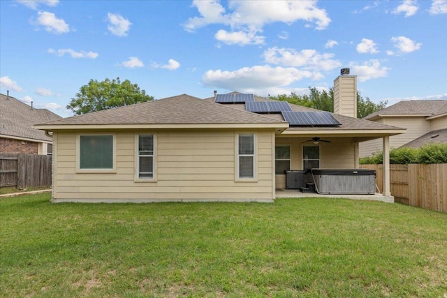 rear view of house with a fenced backyard, a lawn, a ceiling fan, a hot tub, and roof mounted solar panels