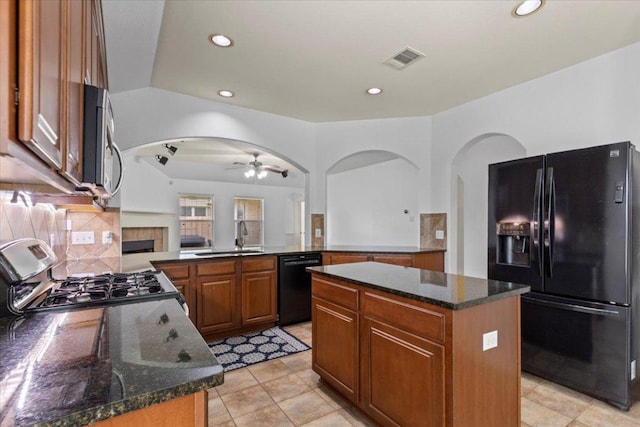 kitchen featuring brown cabinetry, black appliances, ceiling fan, a sink, and a center island