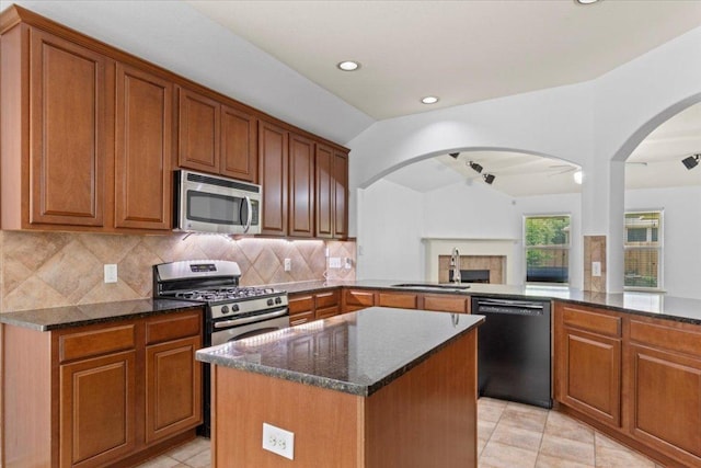 kitchen featuring a sink, a fireplace, dark stone countertops, appliances with stainless steel finishes, and lofted ceiling