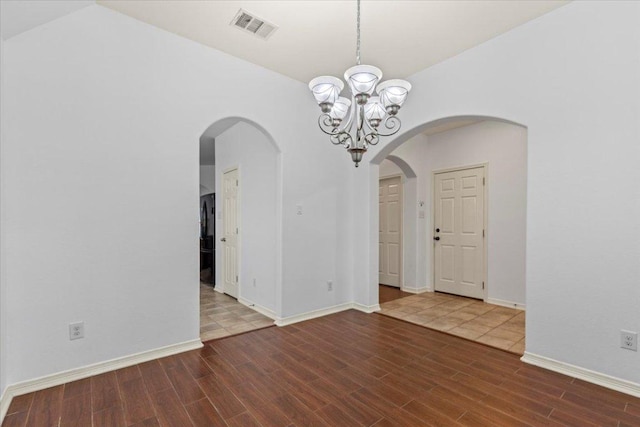 empty room with arched walkways, visible vents, wood finished floors, and a chandelier