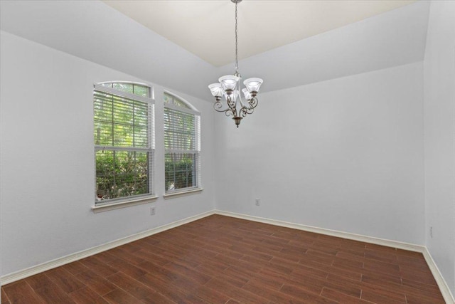 empty room with a notable chandelier, dark wood-style floors, and baseboards